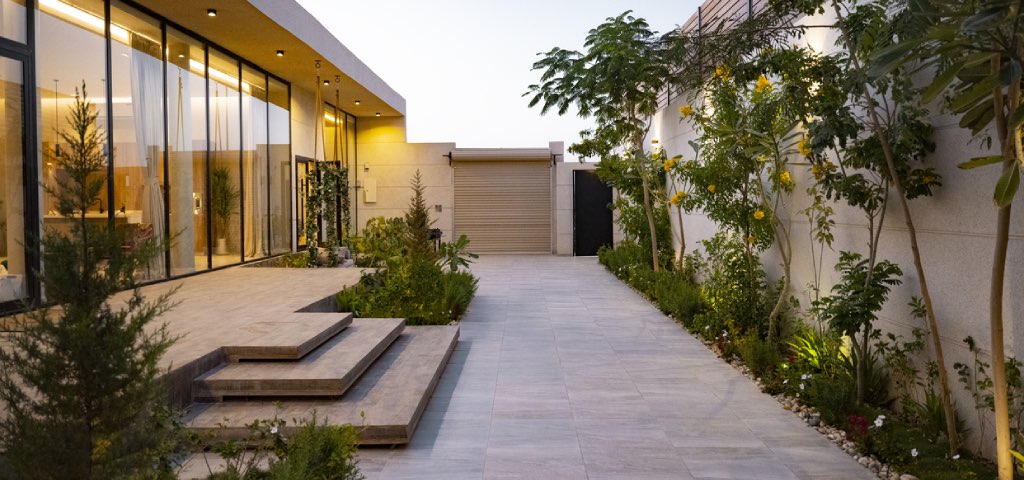 Exterior driveway of a luxury listing that is tree-lined down to the closed garage with an expansive and modern home entryway